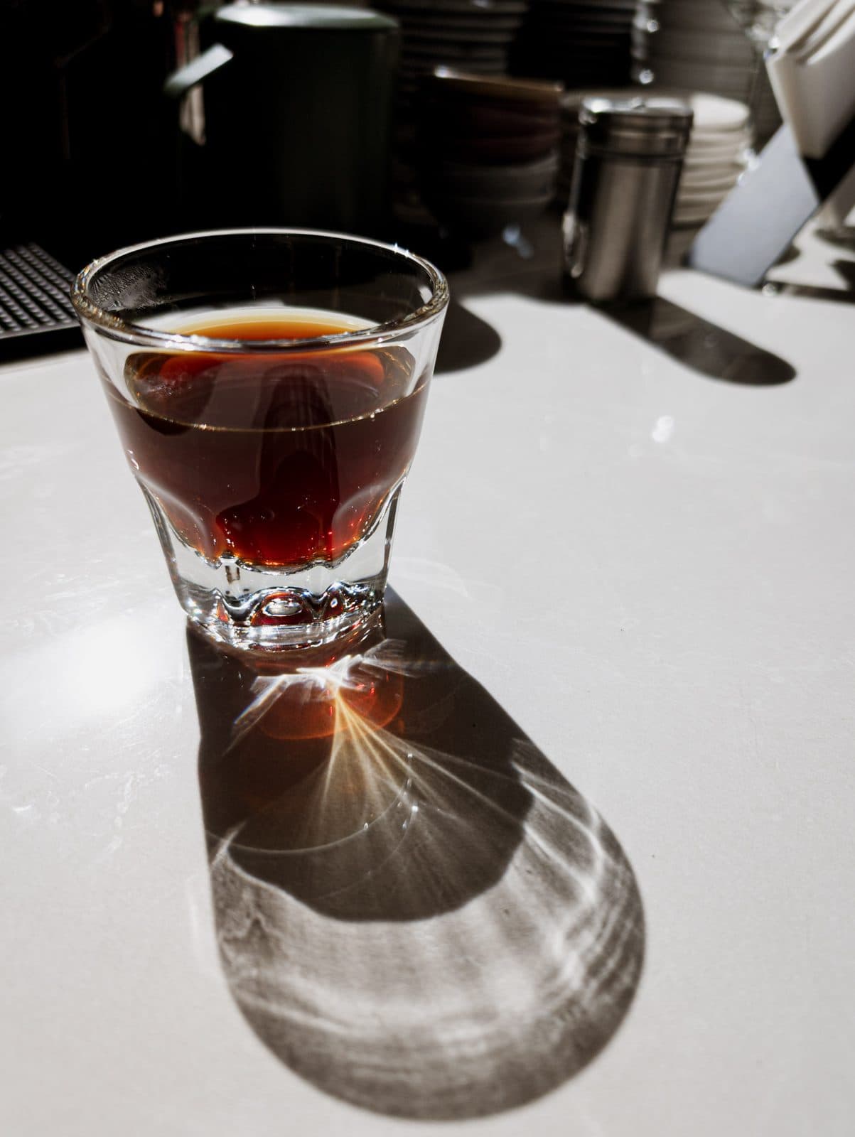 A glass of coffee backlit on the counter, casting its shadow on the table